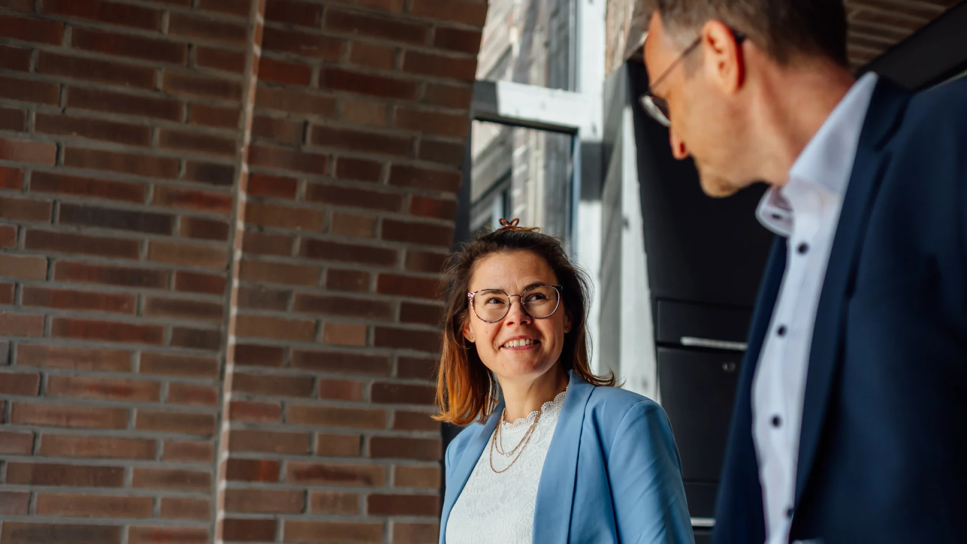 Zwei Personen sprechen am Eingang zum Sitz des Genossenschaftsverbands Weser-Ems miteinander. Das Bild steht für die GVWE Dienstleistungsgruppe und die gebündelten Leistungen des Verbands.
