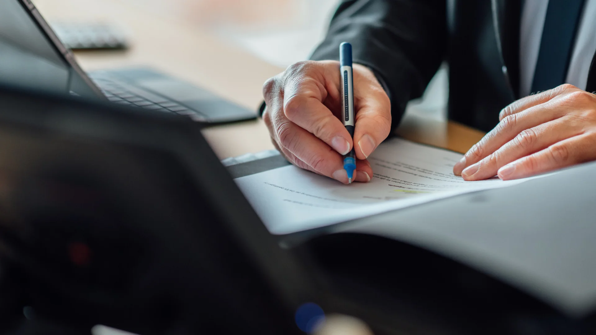 Eine Person markiert mit einem Stift Unterlagen an einem Arbeitsplatz mit Laptop. Das Bild steht für sorgfältige Prüfung und den Beruf Verbandsprüfer beim GVWE.
