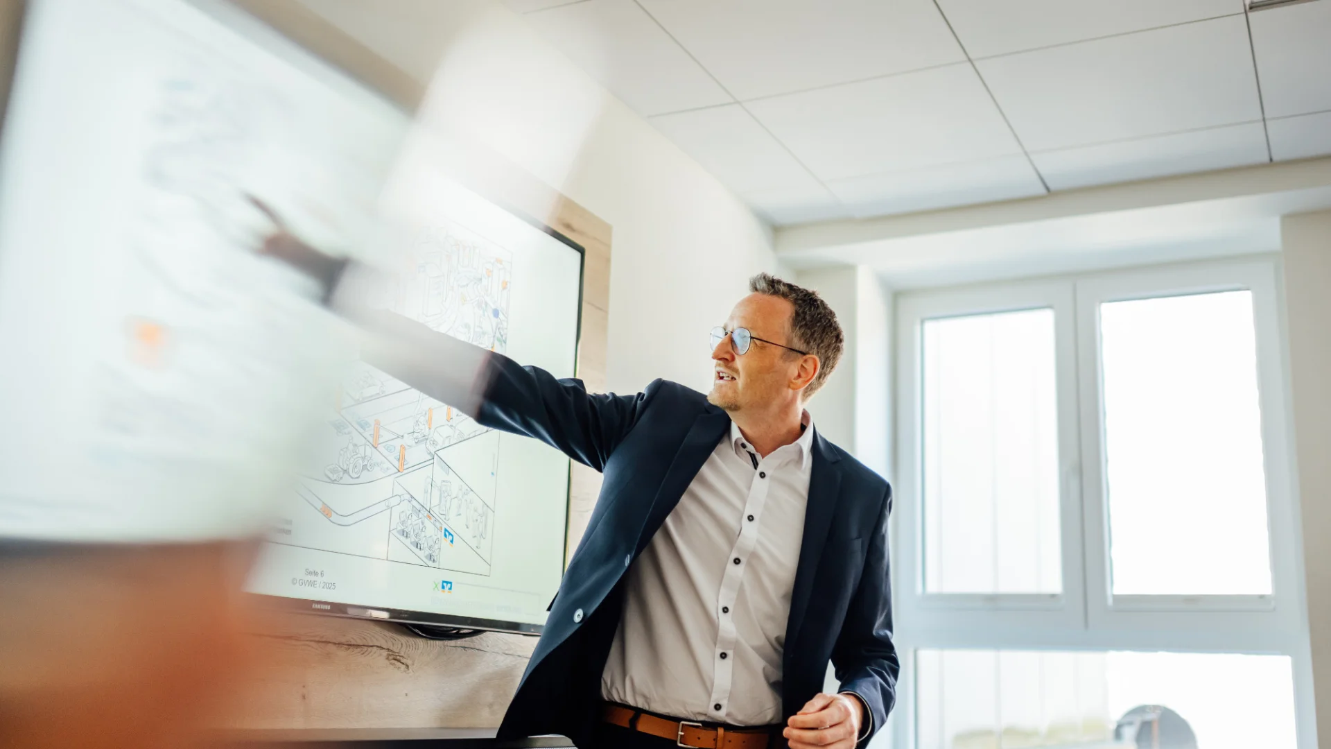 Ein Mann in Geschäftskleidung zeigt in einem Besprechungsraum auf eine digitale Darstellung. Das Bild steht für die strategische Nachhaltigkeitsberatung von Genossenschaftsbanken.