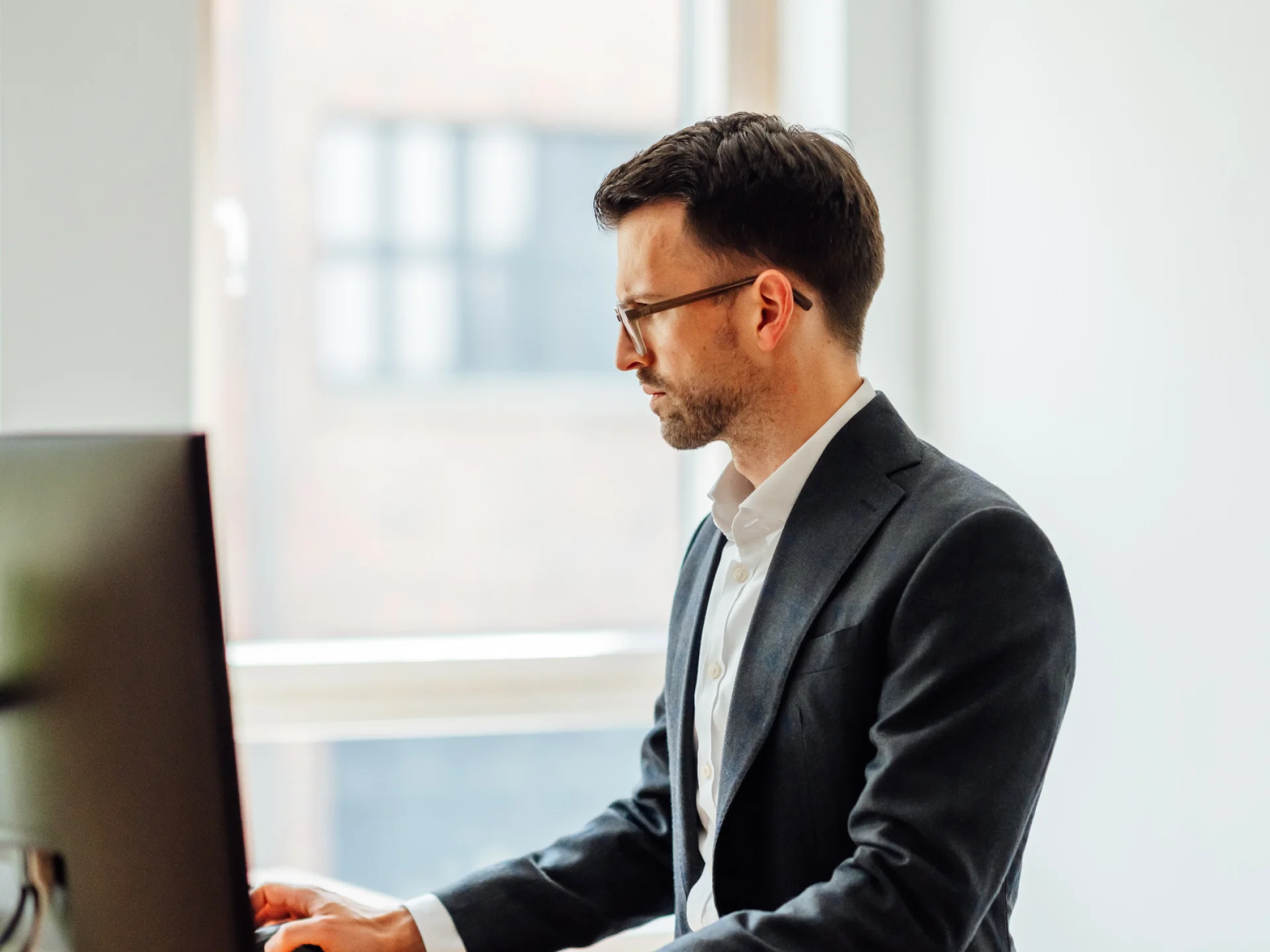 Ein Mann in Geschäftskleidung arbeitet konzentriert an einem Computer in einem hellen Büro.