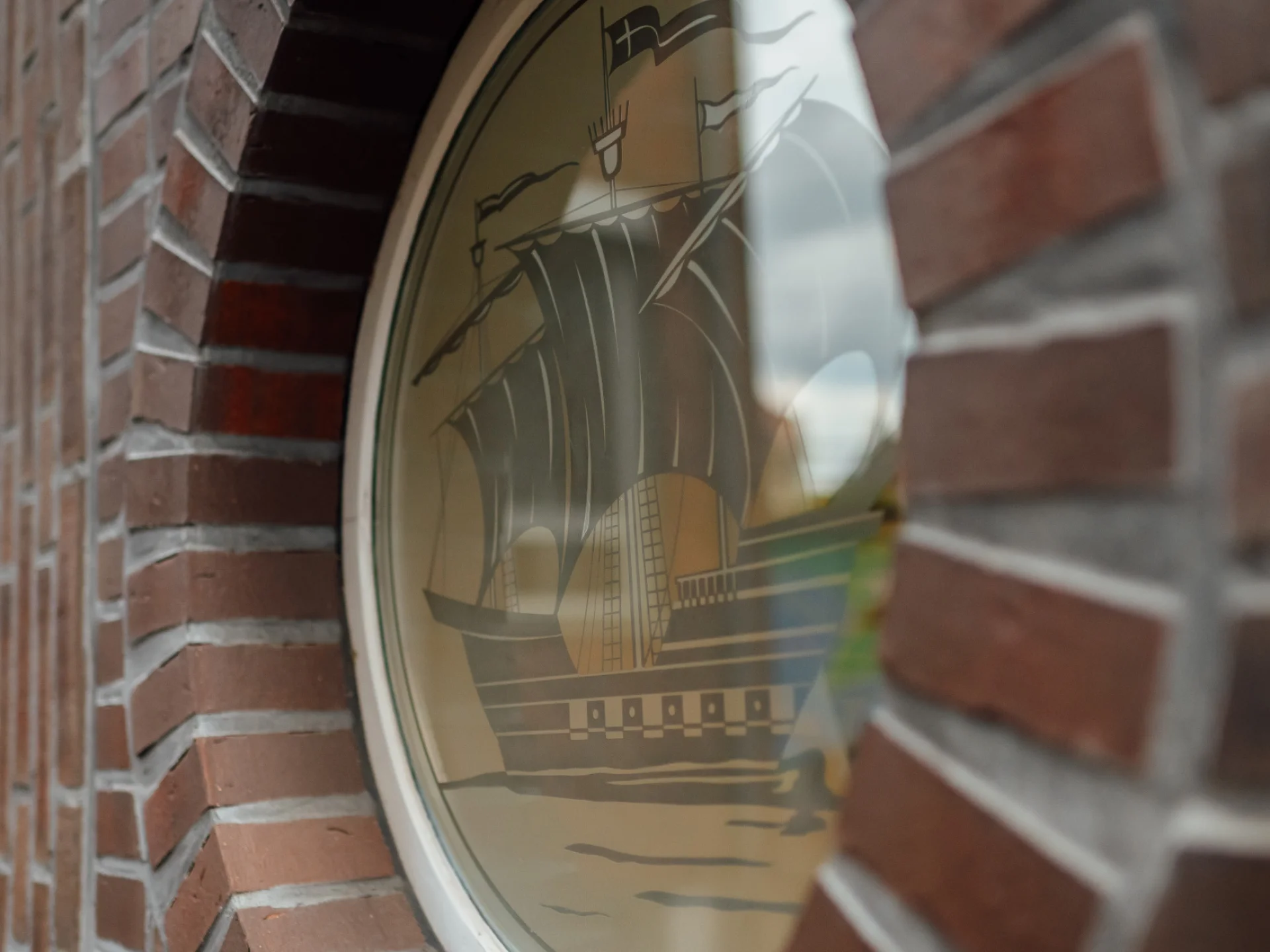 Rundes Fenster mit stilisiertem Schiffsmotiv in einer Backsteinwand am Sitz des GVWE. Das Bild begleitet den Abschnitt zur weiterführenden steuerlichen Beratung von Genossenschaften.