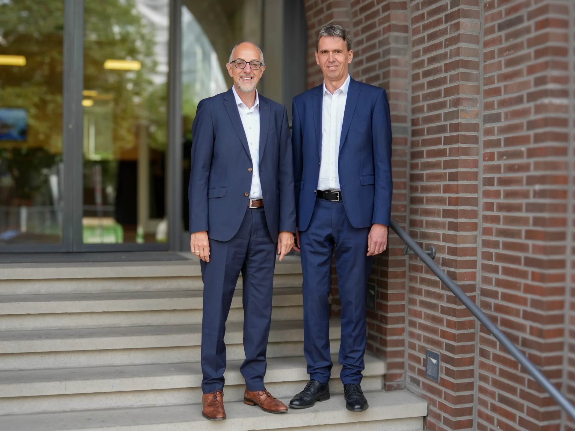 Die beiden Verbandsdirektoren des Genossenschaftsverbands Weser-Ems stehen vor dem Eingang zum Verbandssitz. Das Bild steht für Leitung, Verantwortung und genossenschaftliche Kompetenz im GVWE.