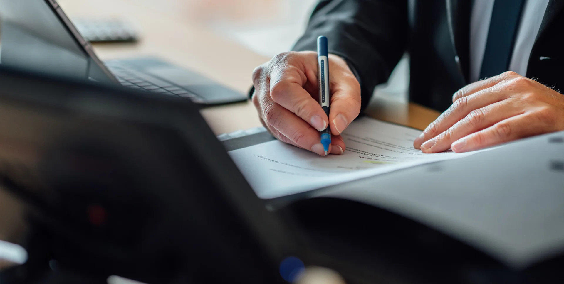 Eine Person markiert mit einem Stift Unterlagen an einem Arbeitsplatz mit Laptop. Das Bild steht für sorgfältige Prüfung und den Beruf Verbandsprüfer beim GVWE.